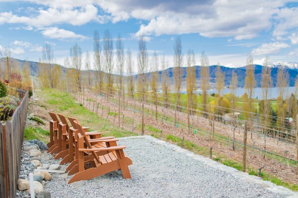 A row of wooden chairs lined up on a gravel path with a mountain and lake in the background.