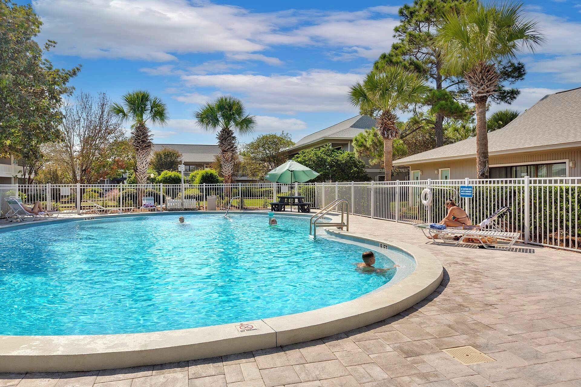 A swimming pool with a white fence, palm trees, and lounge chairs.