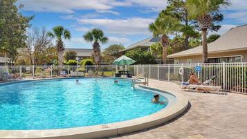 A swimming pool with a white fence, palm trees, and lounge chairs.