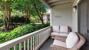 A balcony with wicker furniture and a view of a garden and buildings.