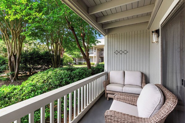 A balcony with wicker furniture and a view of a garden and buildings.