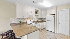A kitchen with white cabinets, a granite countertop, a stove, a microwave, and a refrigerator.