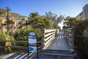 Walk along the well-maintained boardwalk to the beach, flanked by lush greenery and residential buildings.