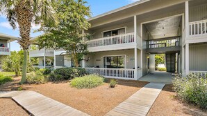 A two-story building with a covered outdoor area, a wooden deck, and a palm tree.