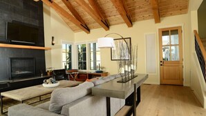 Ein modernes Wohnzimmer mit Kamin, Holzbalken, einer Couch, einem Esstisch und einer Treppe.