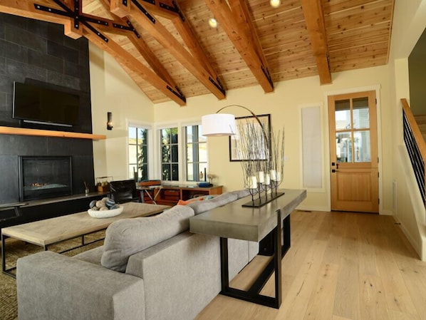 A modern living room with a fireplace, wooden beams, a sofa, a dining table, and a staircase.