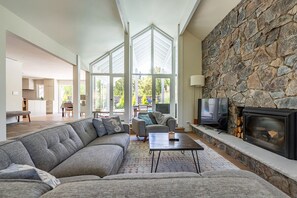 A spacious living room with a stone fireplace, large windows, and a modern sofa. - 4 BR California Living, Heated Pool 80F, Central AC, Pet, West Bellevue, 30d+ ok (Clyde Hill)