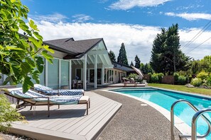 A swimming pool with lounge chairs, a covered patio, and a view of trees. - 4 BR California Living, Heated Pool 80F, Central AC, Pet, West Bellevue, 30d+ ok (Clyde Hill)
