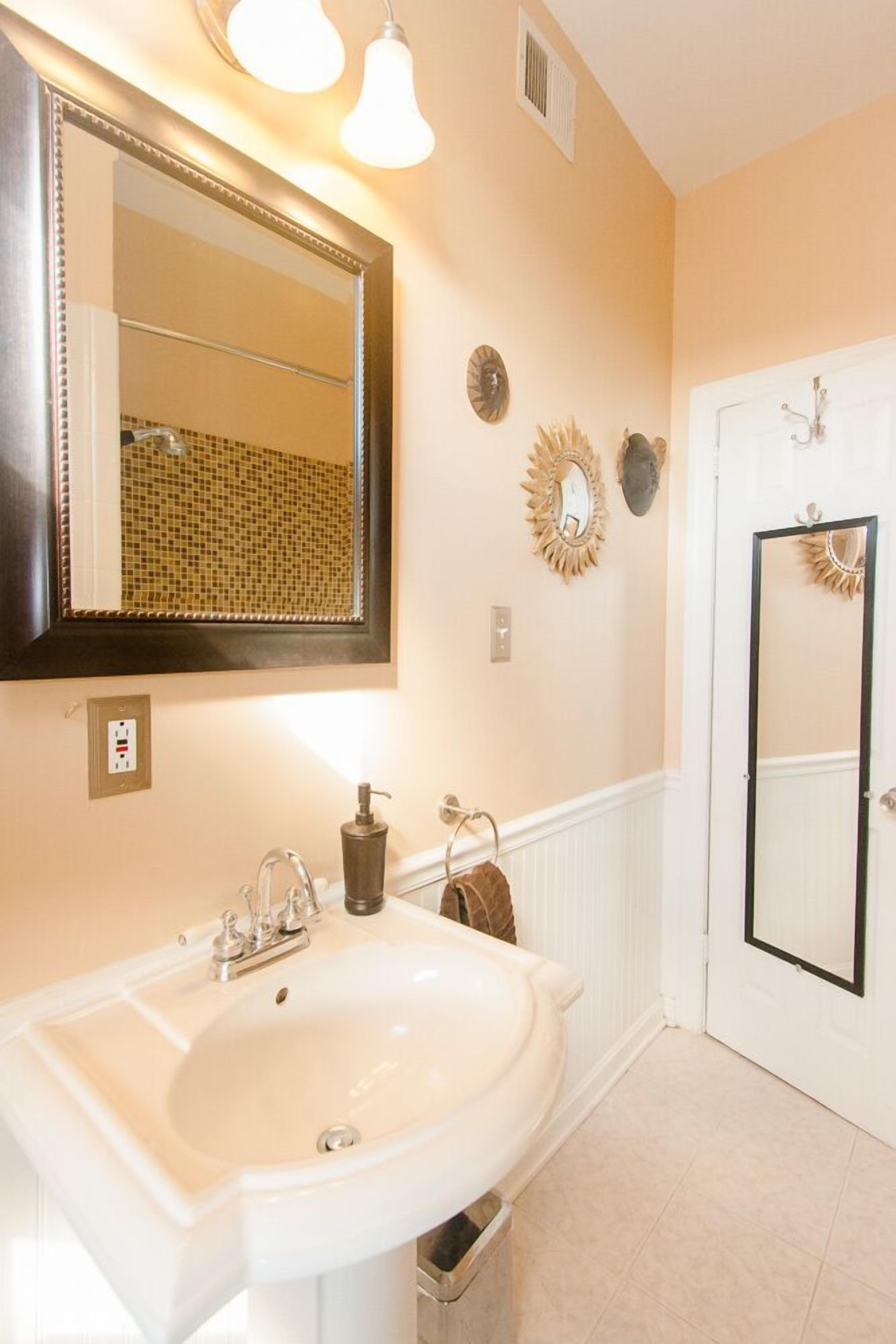 A bathroom with a large mirror, a sink, and a door with a mirror.