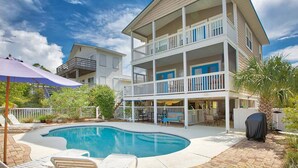 A multi-story house with a pool, outdoor furniture, and a covered patio area.