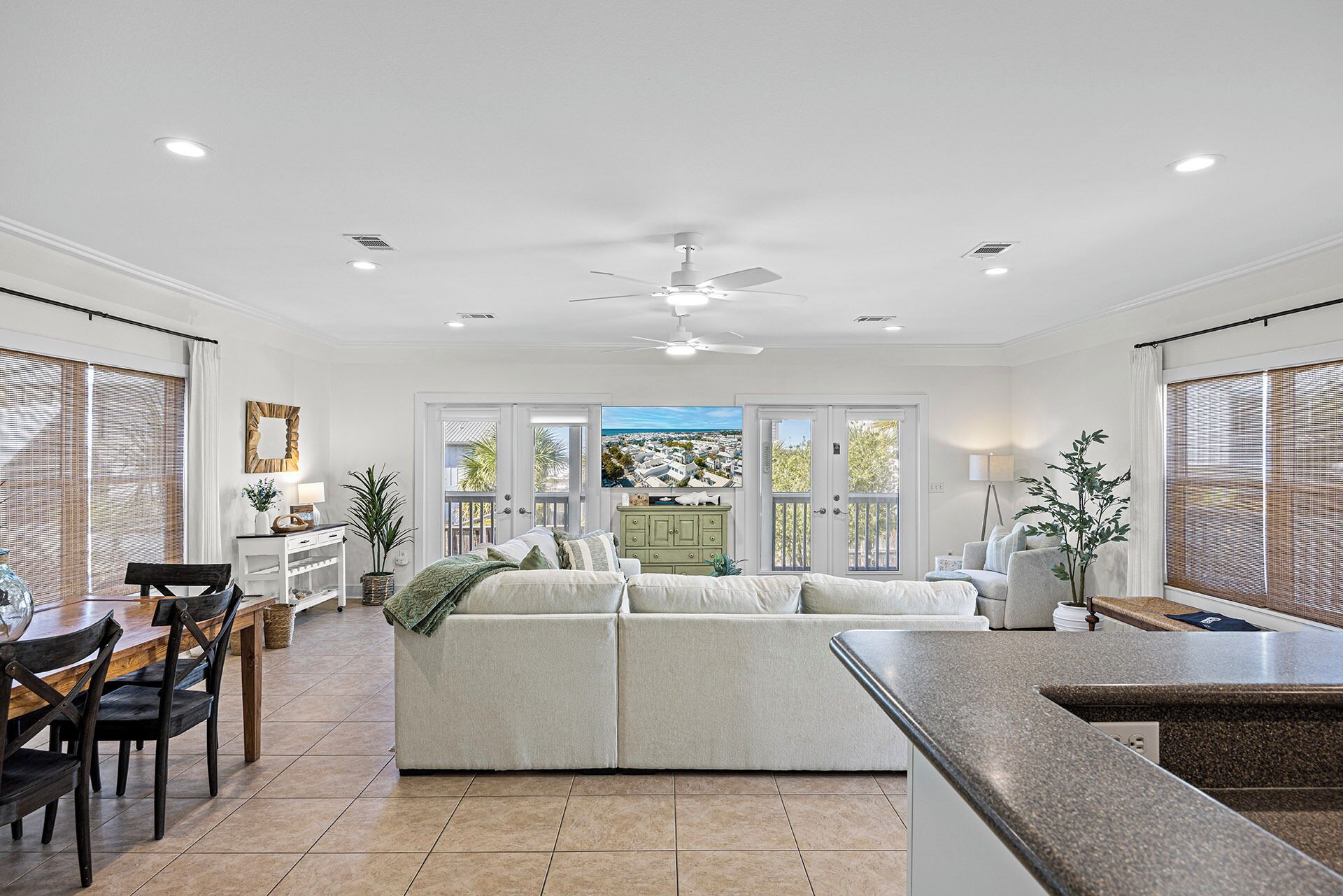 A spacious living area with a large sofa, dining table, and chairs. There is a kitchen area with a countertop and a ceiling fan.