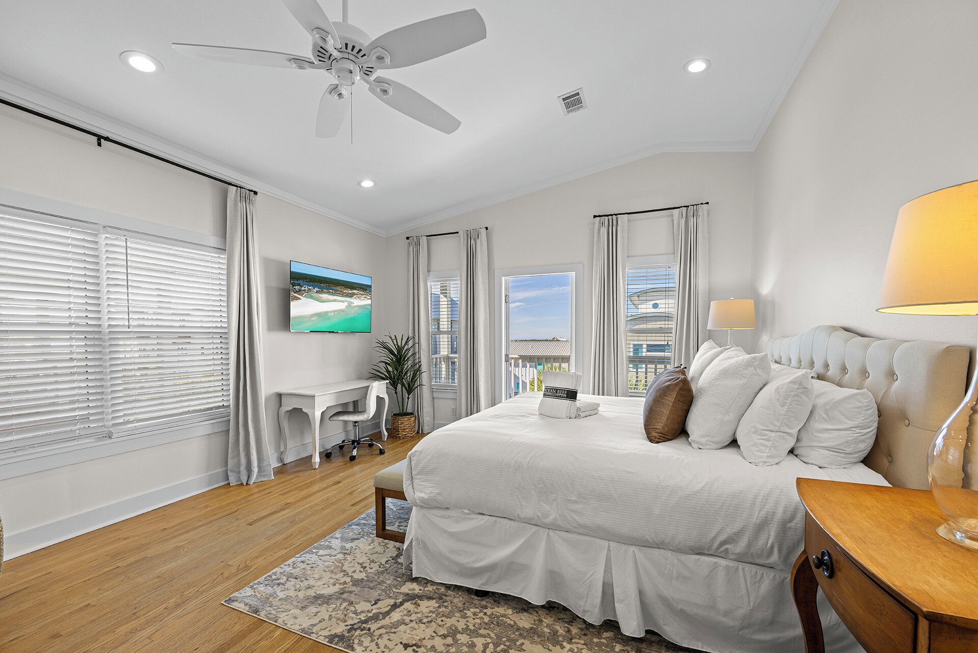 A bedroom with a bed, a desk, a TV, and a ceiling fan.
