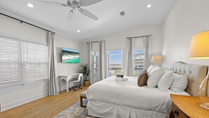 A bedroom with a bed, a desk, a TV, and a ceiling fan.