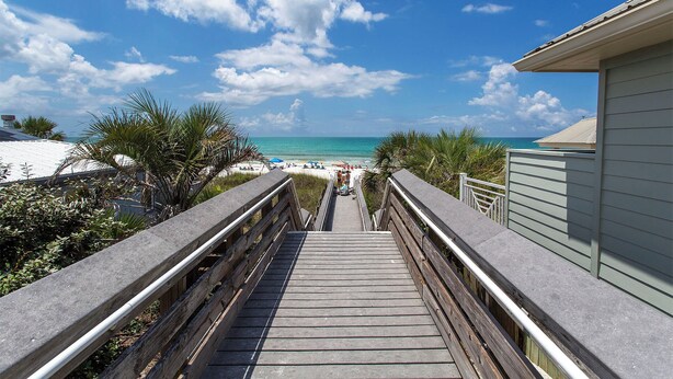 A wooden boardwalk leading to a beach with clear skies and palm trees.