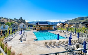 Una piscina con sillas de descanso y sombrillas, rodeada de casas modernas con vistas a las montañas.