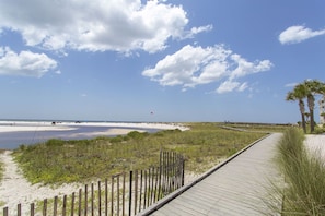 A wooden boardwalk leading to a beach with a sandy shore and a few palm trees.