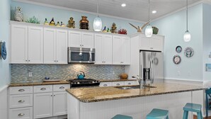 Eine moderne Küche mit weißen Schränken, einer Granit Arbeitsplatte, einem Edelstahlkühlschrank und einer blauen Kochinsel mit Barhocker.