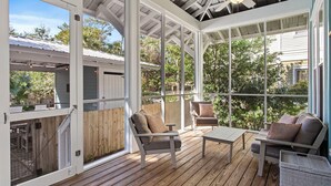 Eine überdachte Terrasse im Freien mit Holzboden, zwei Sofas und einem Tisch.