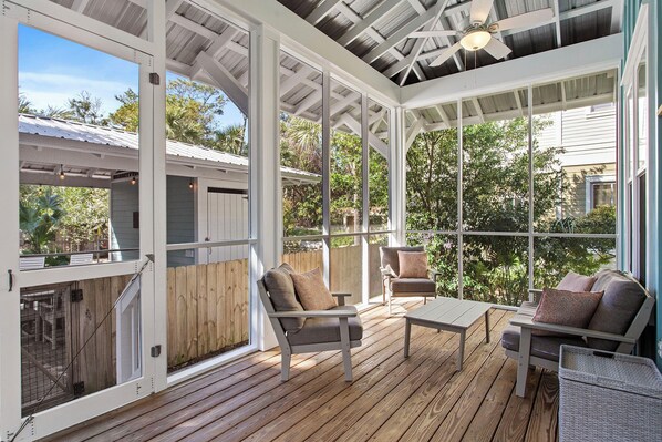 A covered outdoor deck with wooden flooring, two sofas, and a table.