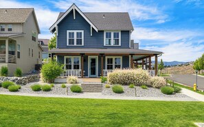 A two-story house with a porch, a stone retaining wall, and a well-maintained lawn.