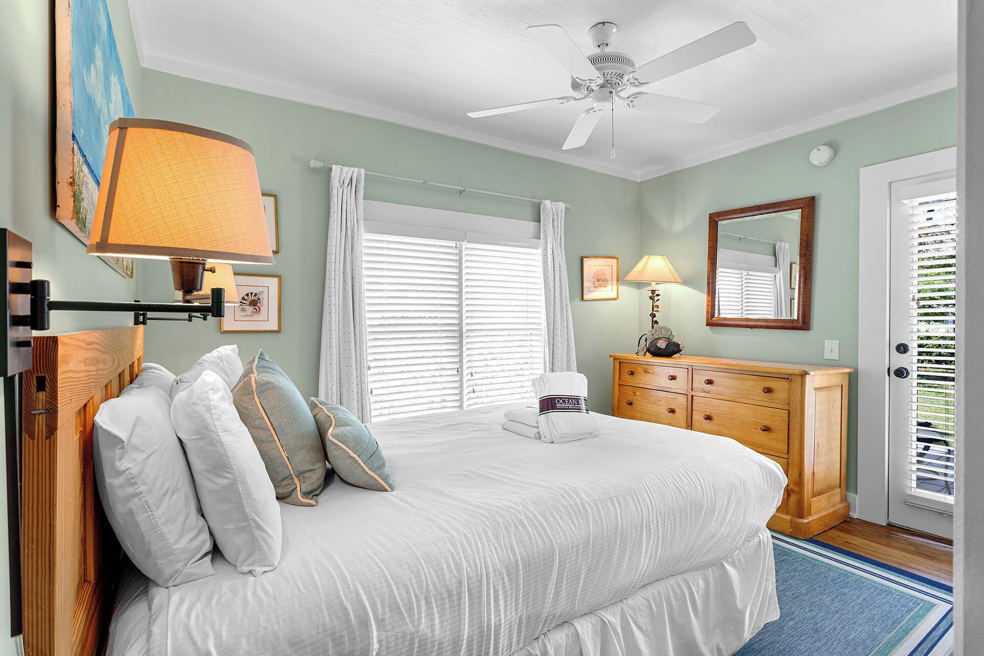 A bedroom with a bed, a nightstand, a dresser, a ceiling fan, and a window with blinds.