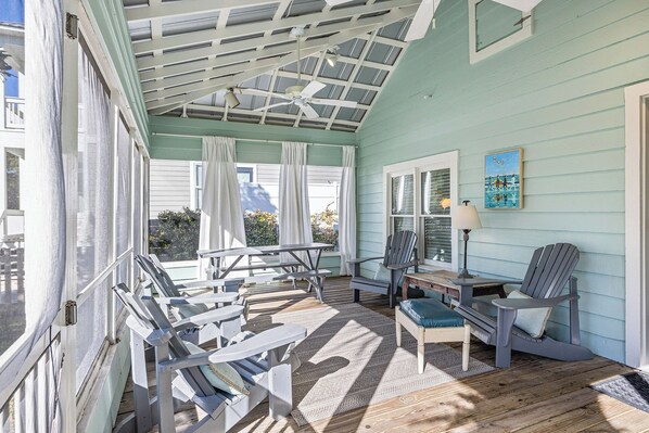 A covered porch with Adirondack chairs, a table, and a ceiling fan.