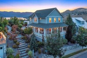 A two-story house with a porch, a stone pathway, and a view of mountains.