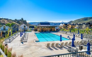 Une piscine entourée de chaises longues et de parasols, elle-même bordée de maisons modernes offrant une vue sur les montagnes.