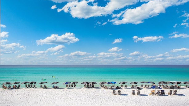 A beach with white sand, clear turquoise water, and a clear blue sky with scattered clouds.