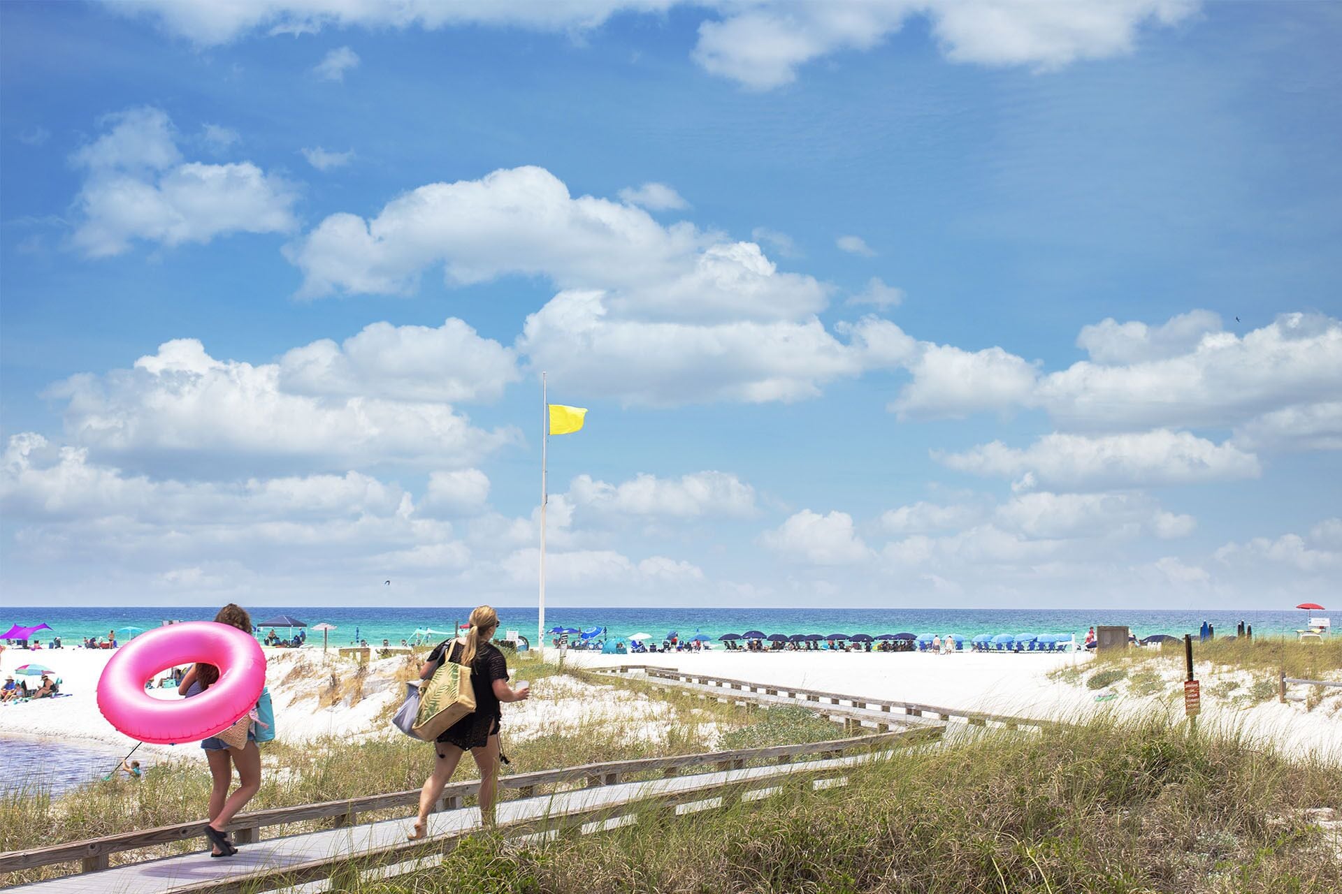 A beach with a wooden boardwalk, a yellow flag, and beach umbrellas.