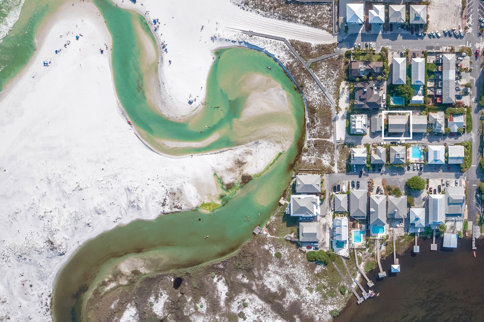 An aerial view of a coastal resort with a sandy beach, a marina, and modern buildings with a uniform architectural style.
