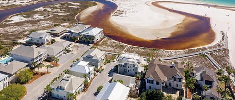 An aerial view of a coastal residential area with houses, a swimming pool, and a beach.