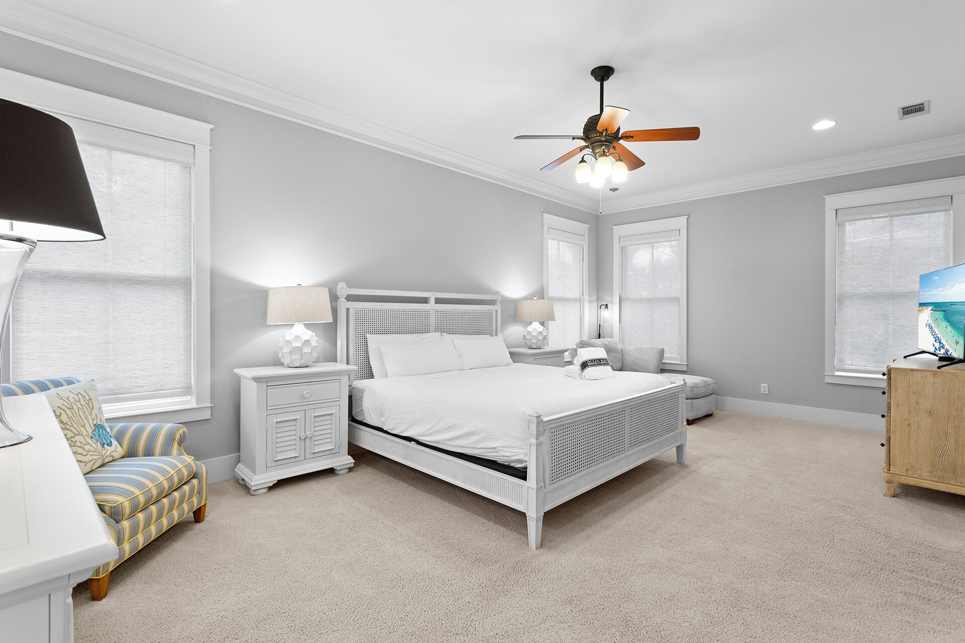 A bedroom with a white bed, two bedside tables, a nightstand, a wooden cabinet, a ceiling fan, and a TV on a wooden stand.
