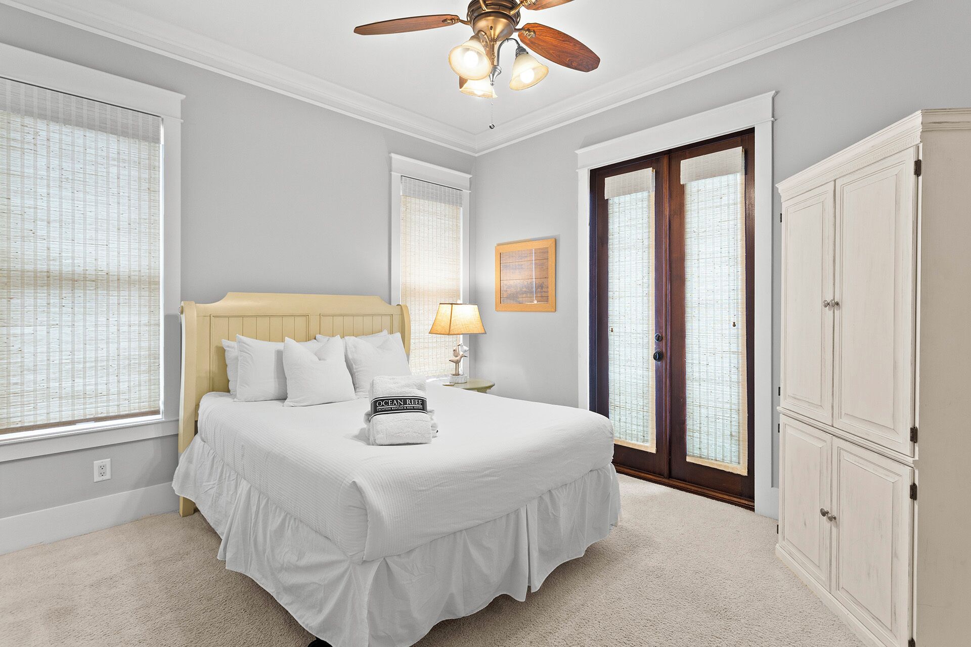 Une chambre à coucher avec un lit, un ventilateur de plafond, une table de chevet avec une lampe, un tableau encadré au mur et une porte avec une fenêtre.