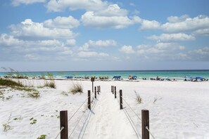 Une plage de sable avec une promenade en bois menant à l’eau, bordée de parasols et de chaises de plage.