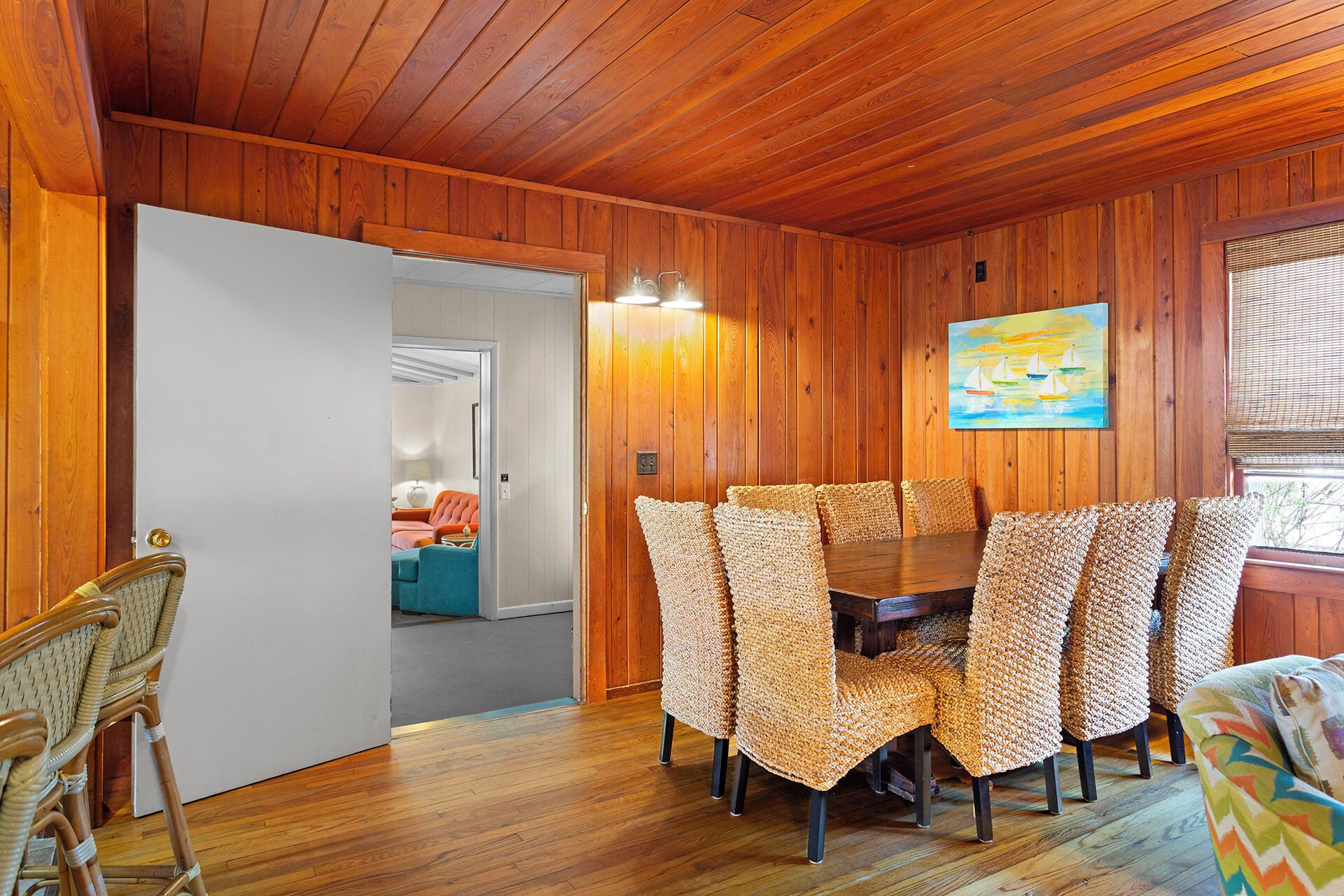 Una habitación con paneles de madera, una mesa de comedor y sillas, un cuadro en la pared y una puerta que da a otra habitación.