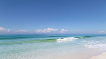 Una playa con agua turquesa cristalina, olas suaves y una orilla arenosa bajo un cielo azul despejado.