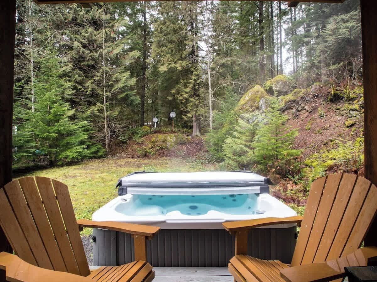 A hot tub with two wooden Adirondack chairs in a forested area.