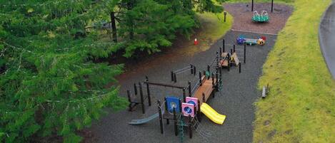 A playground with various play structures, surrounded by trees and a paved path.