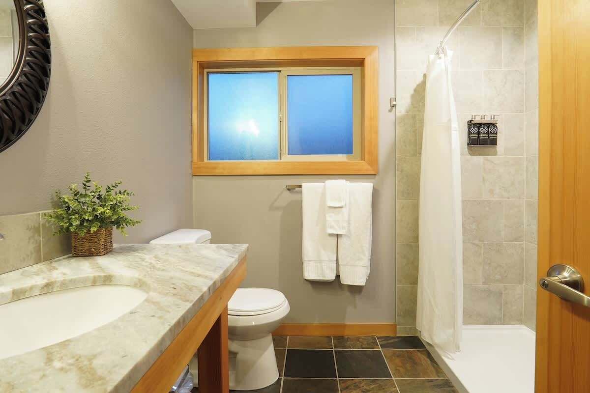 A bathroom with a marble sink, a toilet, a shower, and a window above the toilet.
