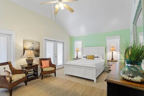 A bedroom with a large bed, a ceiling fan, a chair, a nightstand, and a decorative vase. - Peek A View - Heated Private Pool, Free Beach Service, Walk to Shops + Dining! (Sunrise Beach)
