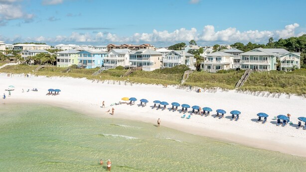 Ett hotell vid stranden med flera våningar, en sandstrand med parasoller och en klarblå himmel.