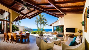 A spacious outdoor area with a dining table and chairs, wicker furniture, and a view of the ocean.