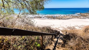 A beach with clear blue water, sandy shore, and a wooden staircase leading down.