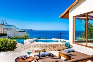 Zona de piscina con sillones de descanso y un jacuzzi de piedra, con vistas al mar azul y cristalino.