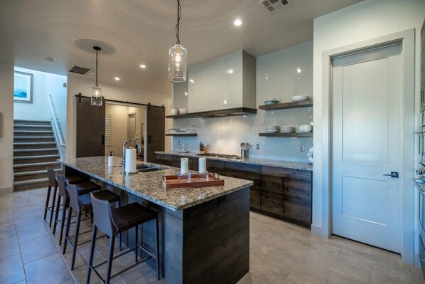 A modern kitchen with a large island, bar stools, and pendant lighting.