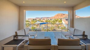 A balcony with seating and a view of a resort area with palm trees and mountains. - Steps to the Pool | Private Hot Tub | Red Rock Views | Arcadia #4 (Santa Clara)
