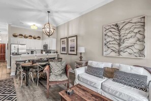 A living room with a dining area, a white sofa, a chandelier, and a large abstract painting.