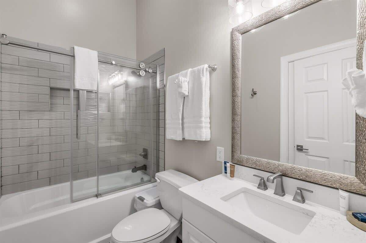 Ein modernes Badezimmer mit Duschkabine aus Glas, einer weißen Toilette, einem Waschbecken mit Spiegel und einer weißen Tür.