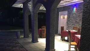 An outdoor dining area with stone pillars and tables covered with red tablecloths.